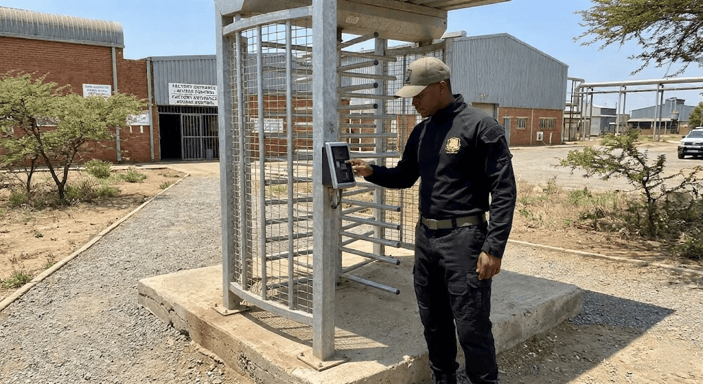 Full-height industrial turnstile gate installed on a concrete base with a biometric reader at a South African factory entrance, representing a factor in total turnstile gate price.